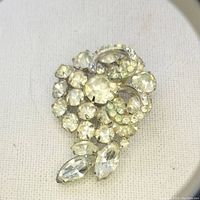 Close-up photo of an Art Deco Weiss brooch featuring clear rhinestones arranged in a floral design with swirl accents on silver-tone metal.