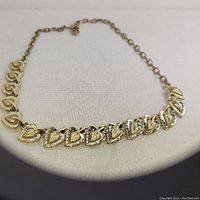 Front view of Coro 1940s vintage leaves and hearts gold-tone necklace laid flat on a cream fabric background.