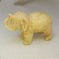 Front angled view of carved jadeite elephant figurine showing trunk, ears, and legs with natural color variations.