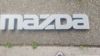 Close-up of Mazda dealership sign letters showing wear and size relative to ground surface.