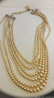 Photo shows the 6-strand graduated pearl necklace laid flat, detailing the graduated sizing of the pearls and the vintage style metal clasp with adjustable chain closure.