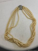 Photo of mid century 5 strand costume pearl necklace laid out on a white fabric surface showing clasp and strands.