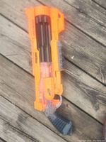 Orange and black Nerf blaster with rotating barrel on wooden surface.