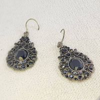 Pair of antique gold-toned teardrop drop earrings with multiple black stones and a larger central black stone, photographed on a white textured fabric.