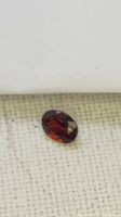 Close-up image of an oval-shaped red faceted tourmaline gemstone on a light surface, showing its color and cut.