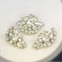 Set of one rhinestone brooch and two matching clip-on earrings laid out on fabric background