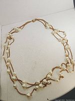 Photo of triple strand vintage style pearl necklace on multi-strand gold-tone chain laid flat to show design and pearl placement