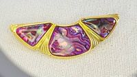 Close-up photo of the vintage brooch showing bright and colorful Paua shell inlaid in a gold-tone metal setting with three segments forming a crescent shape.