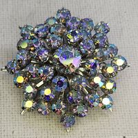 Front view of vintage brooch showing round cluster of iridescent AB rhinestones set in silver-tone metal prong settings on neutral fabric background.