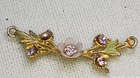 Close-up of elongated gold-tone pendant component with enamel flower and pink rhinestones