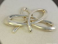 Close-up photo showing the brooch's back pin and loop intersections on light fabric background.