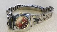 Photo showing angle of steel watch with red dial, gold hands, and steel linked bracelet.