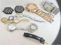 Nine assorted wristwatches showing different styles, sizes, and bands, arranged on white surface.
