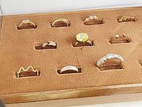 Eleven assorted rings displayed on a brown soft insert tray showing various designs, stones, and metals.