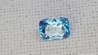 Close-up photo of the loose cushion cut blue topaz gemstone showing facets and color.