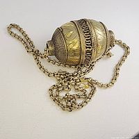 Necklace with ornate oval pendant showing gold leaf and swirl motifs, chain laid loose around pendant.