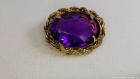 Close-up front view of the vintage purple brooch showing the oval faceted purple stone and gold-tone rope bezel setting