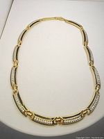 Full view of the necklace laid flat showing the gold-tone links with black enamel and clear rhinestone embellishments.