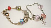 Two charm bracelets laid flat showing colorful and pink glass beads with heart charms.