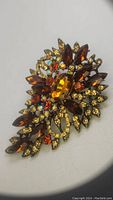 Close-up image of the vintage amber rhinestone statement brooch showing the large central amber oval rhinestone surrounded by marquise-shaped amber stones and smaller orange, yellow, and iridescent rhinestones in a gold-tone metal setting.