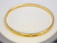 Gold-tone Monet bangle bracelet viewed flattened against light background showing diamond pattern texture.