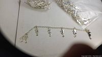 Image showing silver-tone chain bracelet laid flat with multiple seahorse charms and a clasp, partially obscured edges and plastic bags in background.