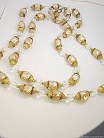 Long baroque pearl necklace laid out showing the pearls, gold-tone bead caps, and clear faceted beads linking pearls.