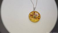 Close-up photo of the round yellow resin pendant with embedded flower design on silver chain.