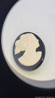 Front view of the vintage oval cameo brooch showing the cream female profile on black background.