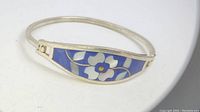 Side view of the silver bracelet with blue inlay and white flower design, showing the hinge and clasp.