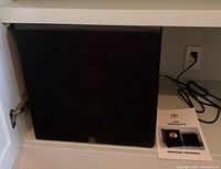 Front view of black ASW subwoofer and owner's manual placed on shelf