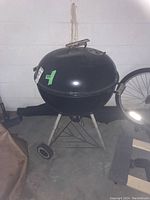 Weber charcoal kettle BBQ grill on metal tripod stand with two wheels and black cover