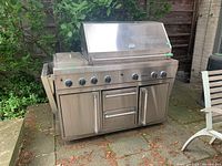 Front-facing view of entire grill on stone patio beneath tree