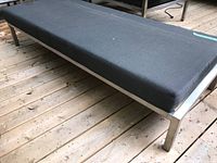 Full view of bench with black upholstered cushion mounted on a silver metal frame, positioned on outdoor wooden deck.