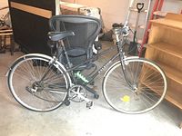 Side view of the entire Raleigh men's road bicycle with visible black frame, white wall tires, and saddle shown indoors in garage setting.