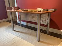 Side angle showing the wood veneer desktop with silver metal legs and horizontal support rods.