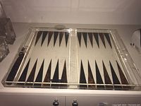 Full view of the plexiglass backgammon board showing the triangular pattern and clear compartments.