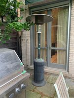 Full view of the tall black patio propane heater with metal reflector top, placed on outdoor patio near sliding glass doors and grill.