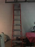 Full view of the aluminum extension ladder showing it upright against a white wall, orange color, two sections visible.