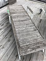 Top-down view of aged wooden lounger with metal frame and wheels on wooden deck.