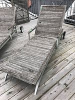 Full view of the lounger showing wood slats and metal frame with wheels on a wooden deck.