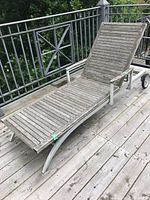 Front perspective view of the lounger on terrace floor showing wood slats and metal frame with wheels