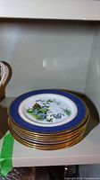 Stack of eight porcelain plates with cobalt blue and gold decorative rims and central painted design featuring cranes and a pagoda.