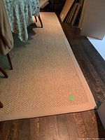 Photo showing the rug laid on a wooden floor with surrounding furniture, showing texture and border.