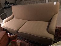 Front-facing view of beige upholstered sofa with two seat cushions on an oriental-style rug, with a dog in the foreground.