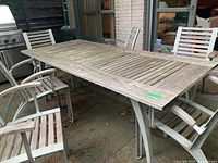 Photo showing the full rectangular wooden and metal table with four matching chairs around it on a patio with outdoor kitchen in background