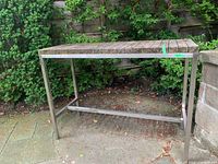 Front view of outdoor wood and metal table showing wood slatted top and metal frame with supporting bars at base.