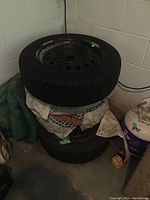Photo of four stacked BF Goodrich tires mounted on steel rims in garage environment, showing general condition and tread wear.