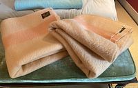 Two folded peach and orange wool blankets on top of a green cushion, showing soft texture and color bands.