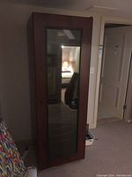 Front view of tall wooden wine cooler cabinet with glass door, placed in a basement room.